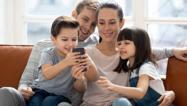 Дигитални родители и децата им гледат екран на телефон и се смеят